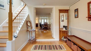 A hallway with a wooden staircase, a rug, and a dining area in the background.