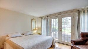 A bedroom with a large bed, a nightstand, a lamp, a window with curtains, and a door leading to a balcony.