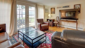A living room with a glass coffee table, leather sofas, a TV, and a large window with curtains.