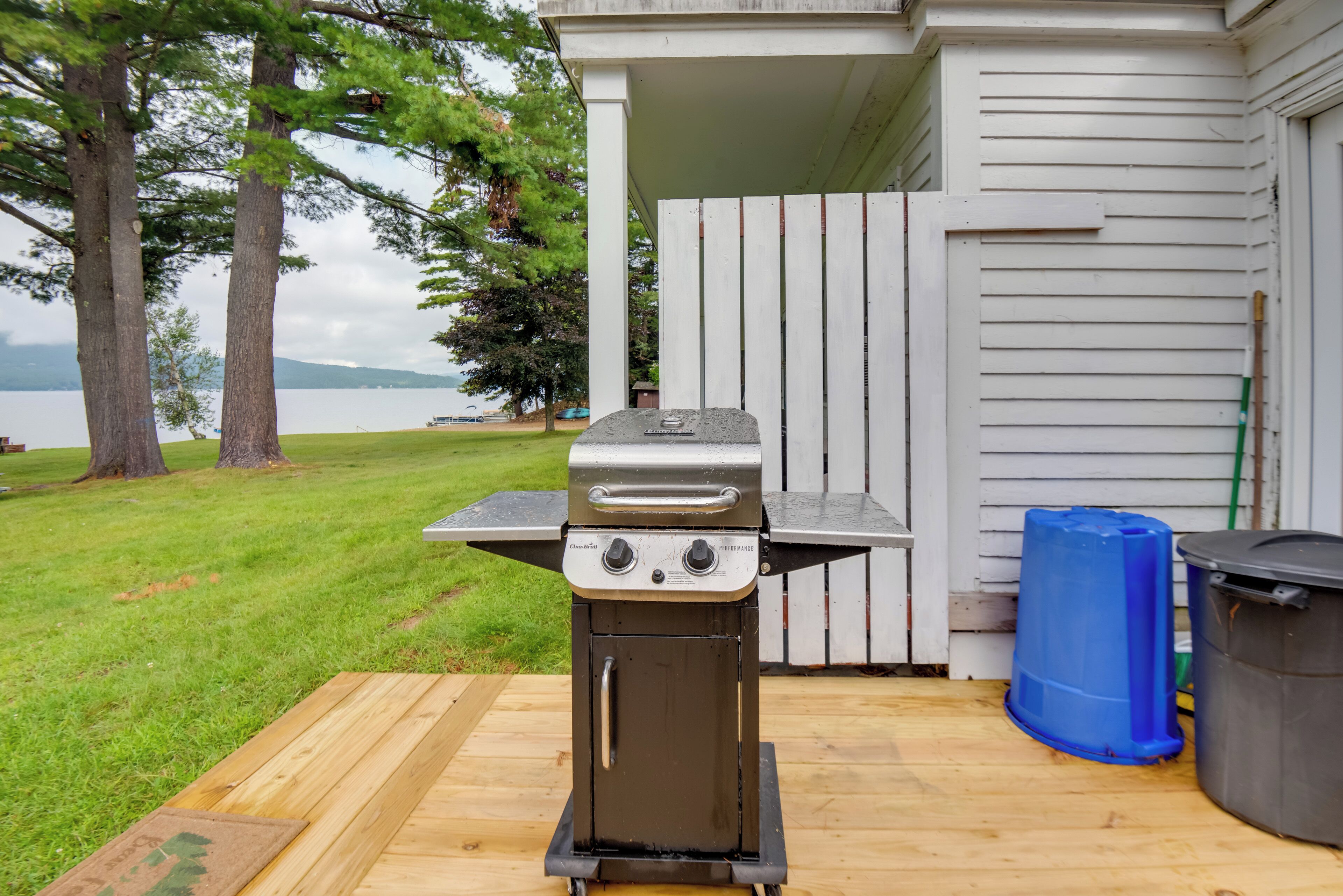 Una parrilla para barbacoa en una terraza de madera con vista a un lago y árboles.