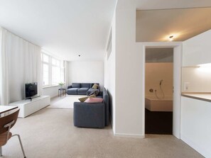 Een moderne woonkamer met een bank, een poef en een televisie op een wit kastje.