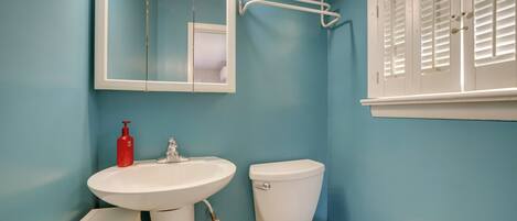 A bathroom with a white sink, a toilet, and a mirror. There is a shelf with toiletries above the mirror.