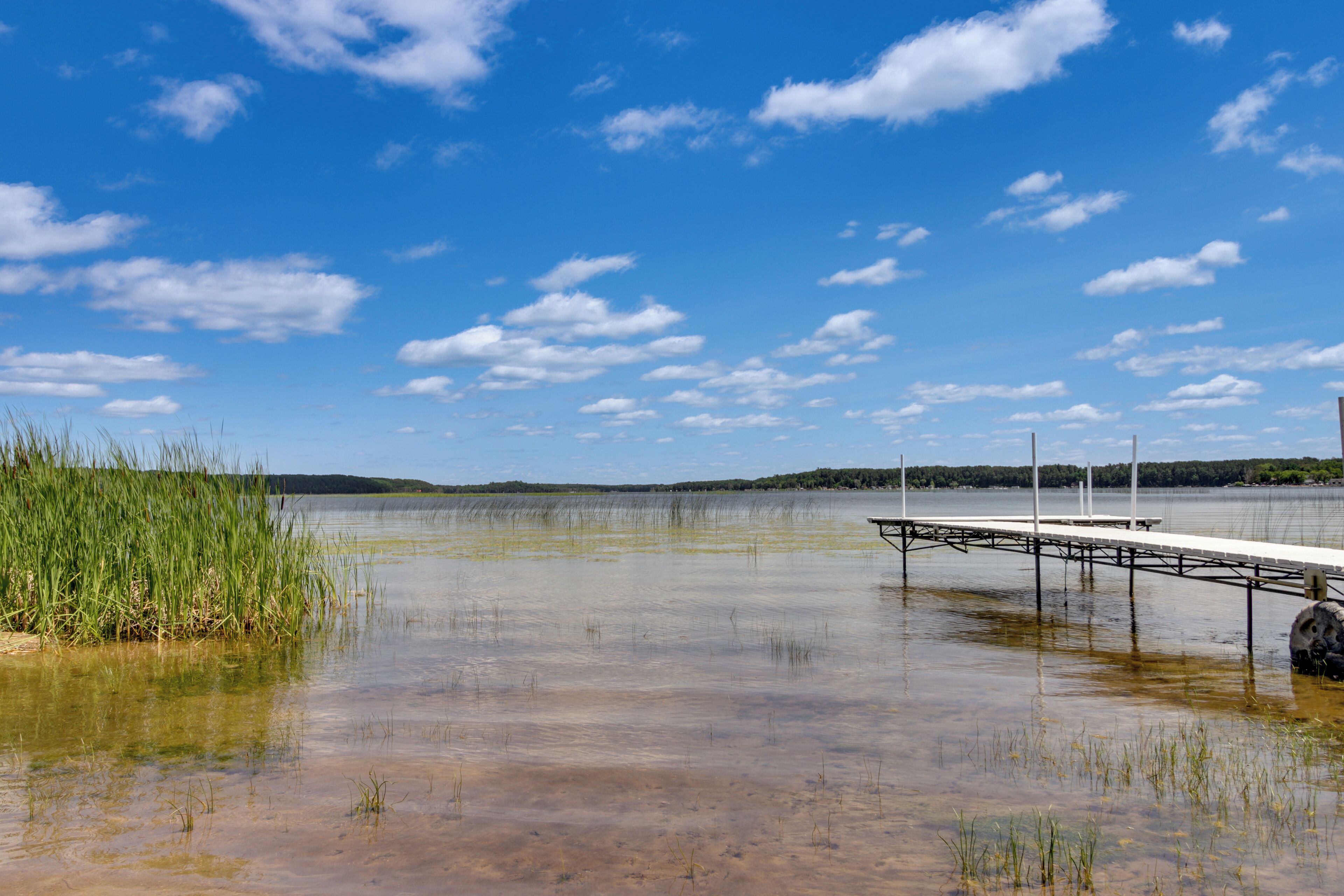 A calm lake with a dock extending into the water, surrounded by grassy areas and a clear sky.