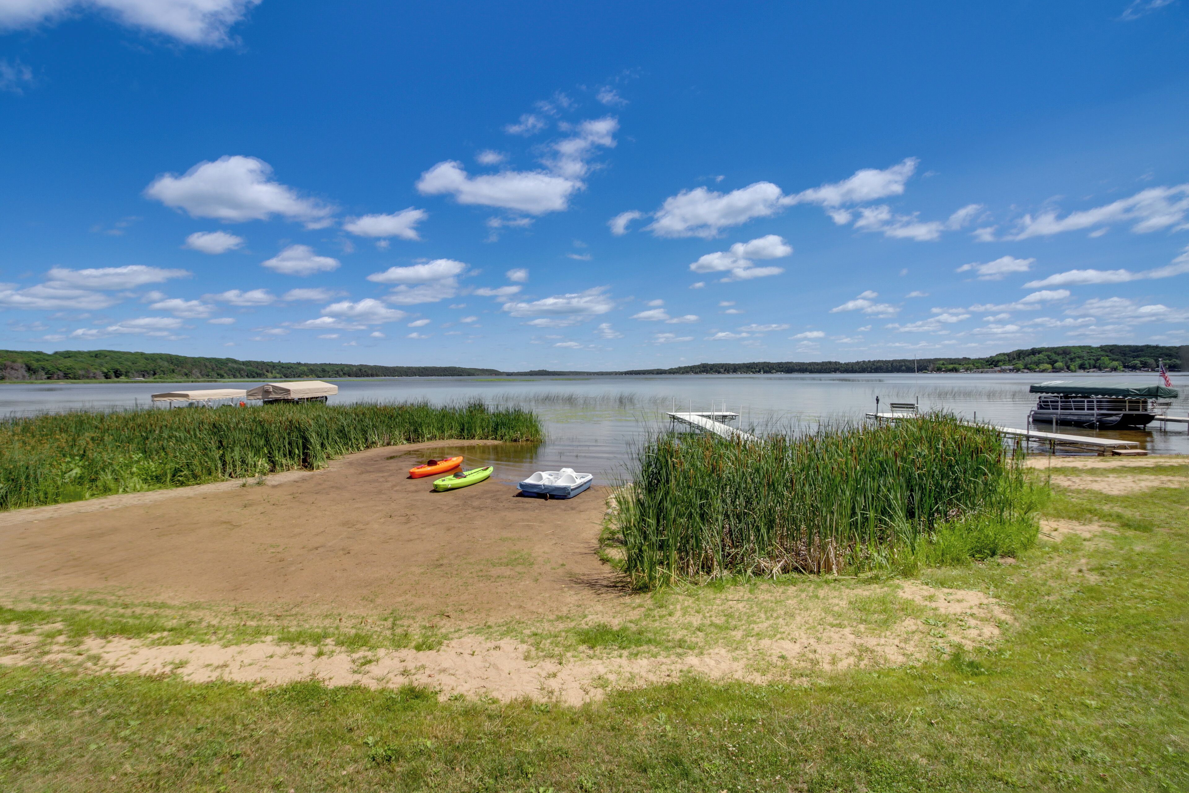A lakeside area with a sandy beach, kayaks, and a dock.