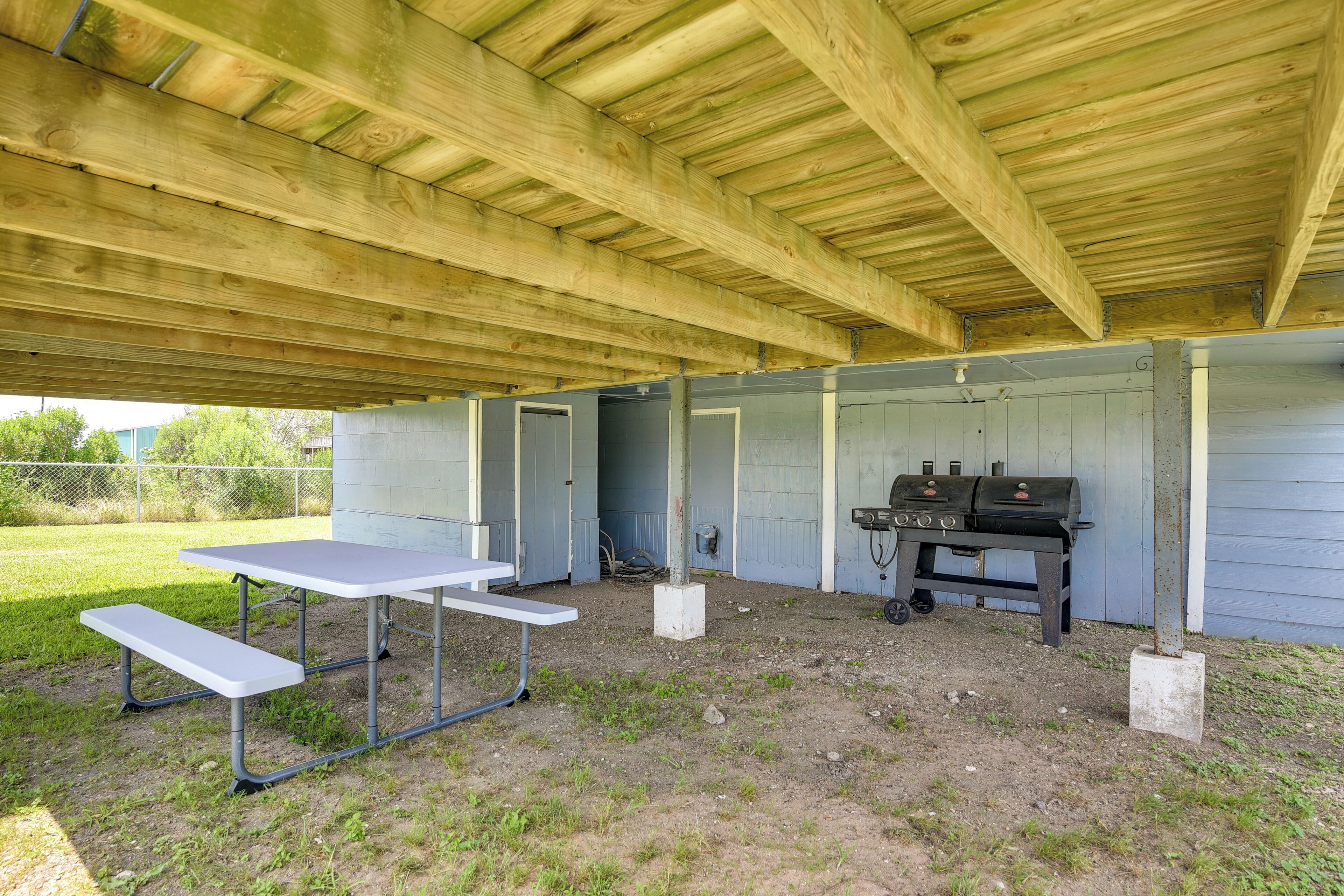 Een overdekt buitengebied met een picknicktafel, barbecue en mobiele toiletten.