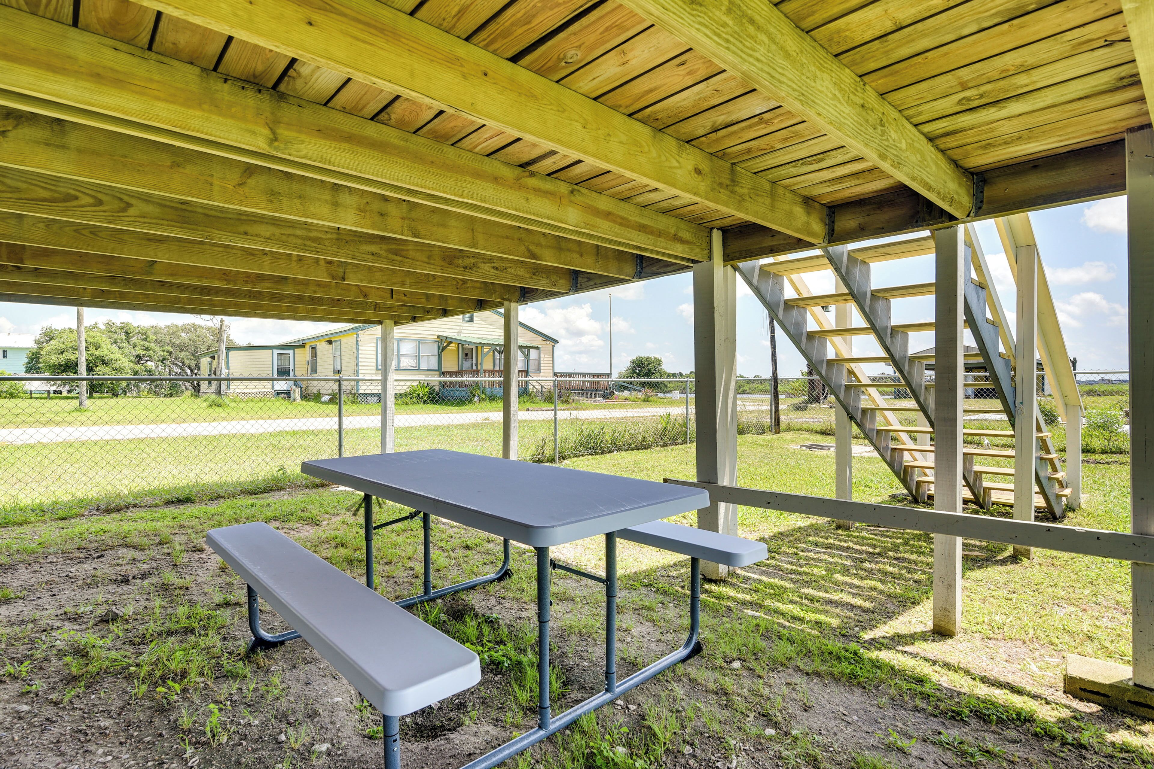 An outdoor covered picnic area with a table and benches, wooden beams, and a staircase.