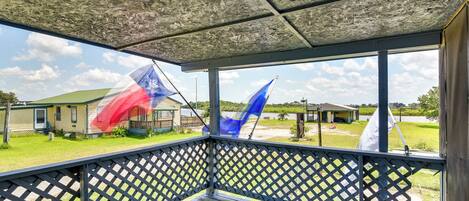A covered porch with a lattice railing, a view of a grassy area, and a house in the background.