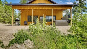 A wooden cabin with a covered porch, a grill, and a chair. - Modern Lakeside Cabin w/ Mountain Views & Hot Tub! (Lakeside)