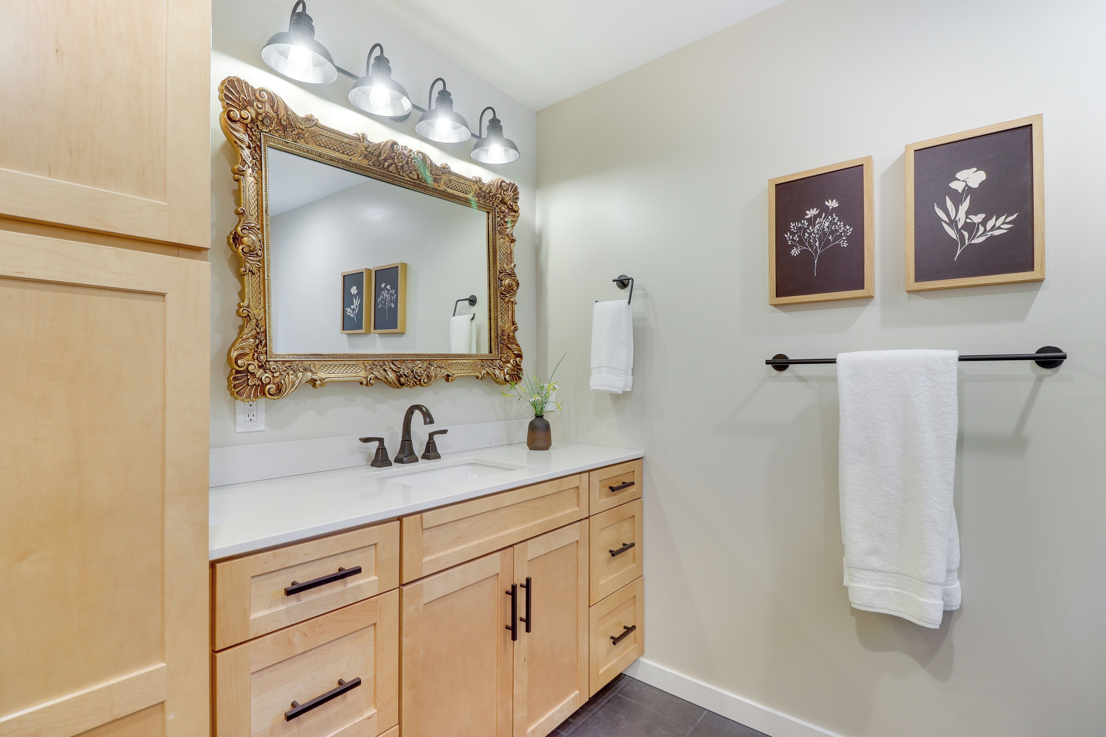 A bathroom with a large ornate mirror, a sink, wooden cabinets, and two framed floral pictures on the wall.