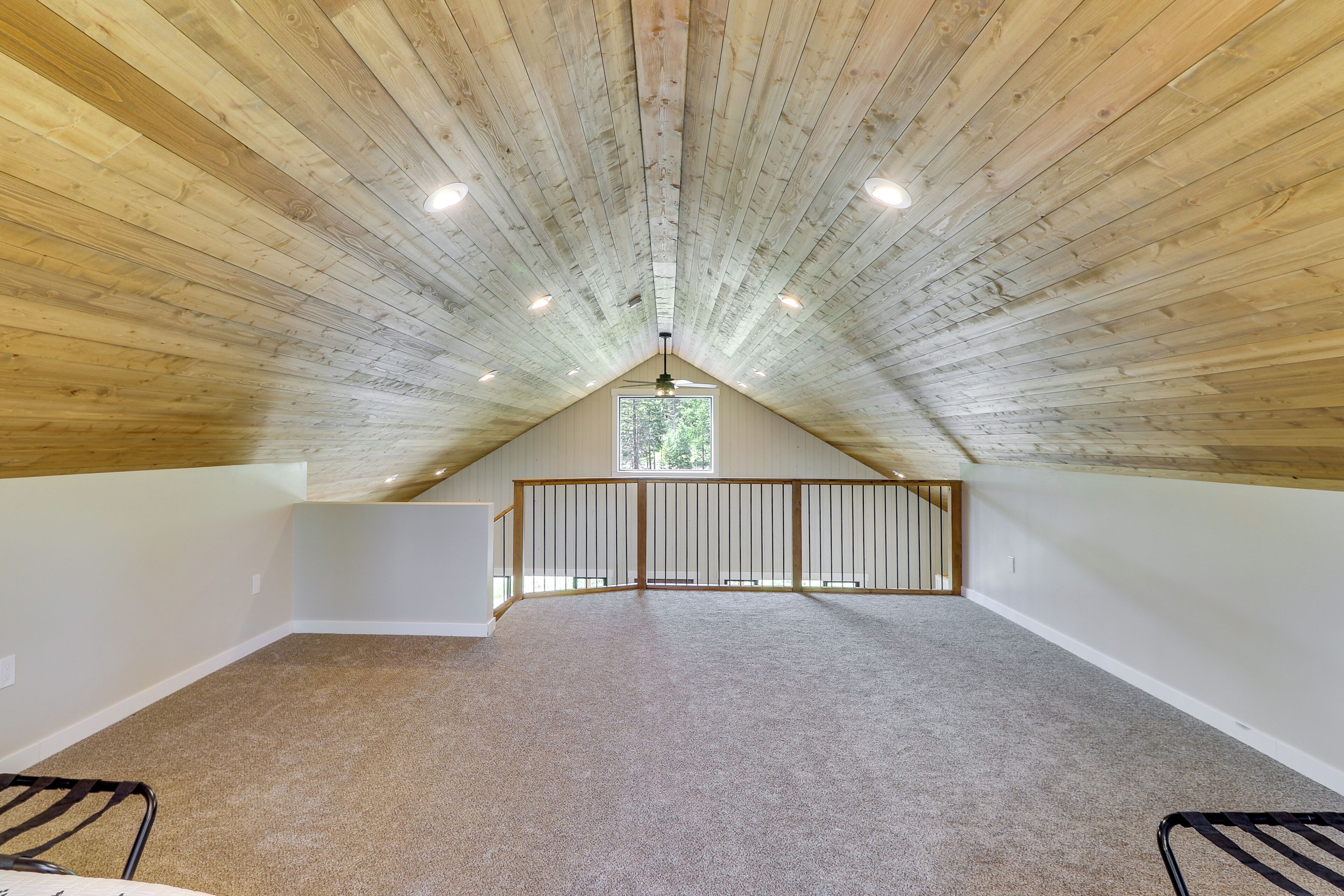An attic room with a sloped ceiling, carpeted floor, and a window with a view of greenery.