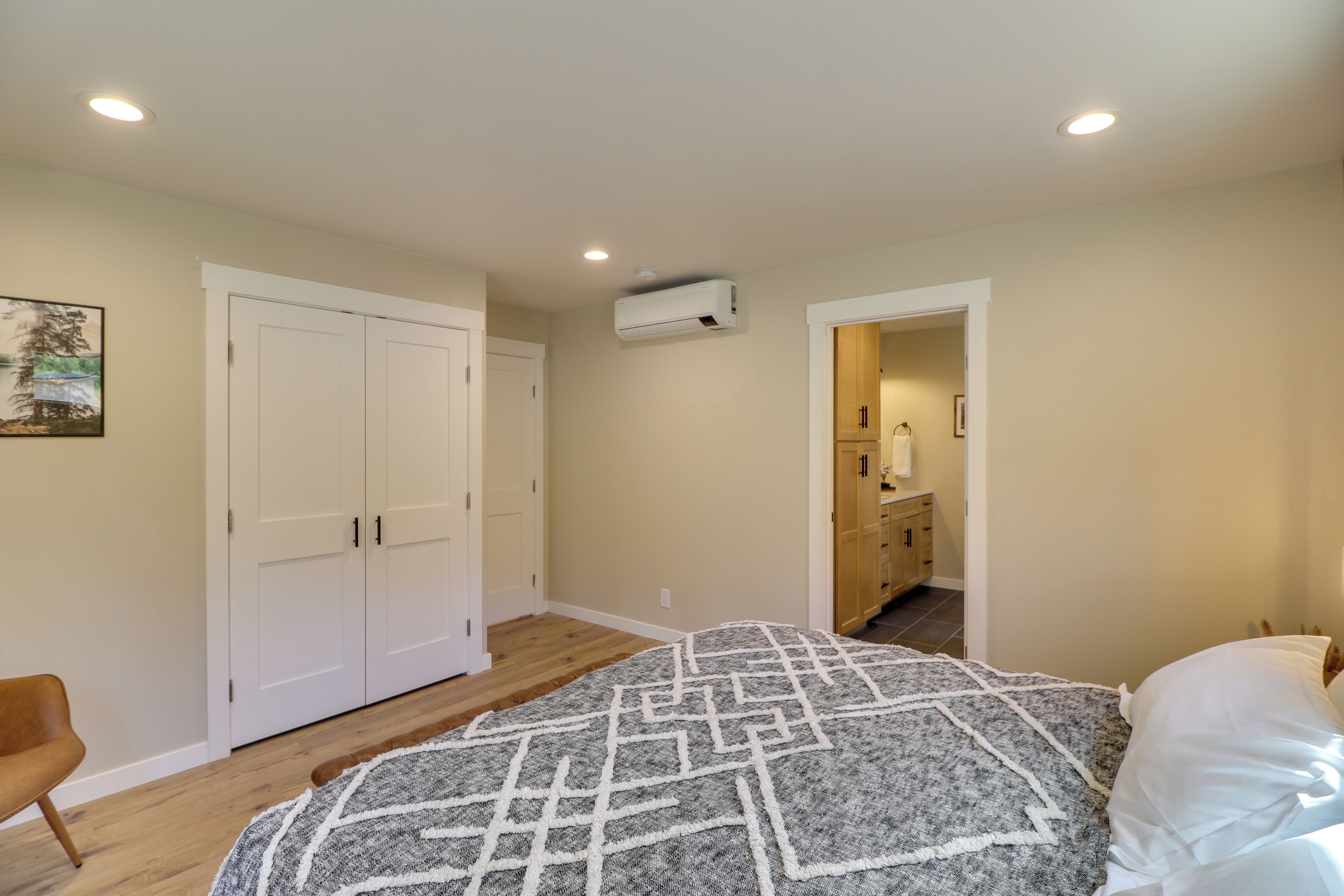 A bedroom with a bed, a wardrobe, an air conditioning unit, and a doorway leading to a bathroom.