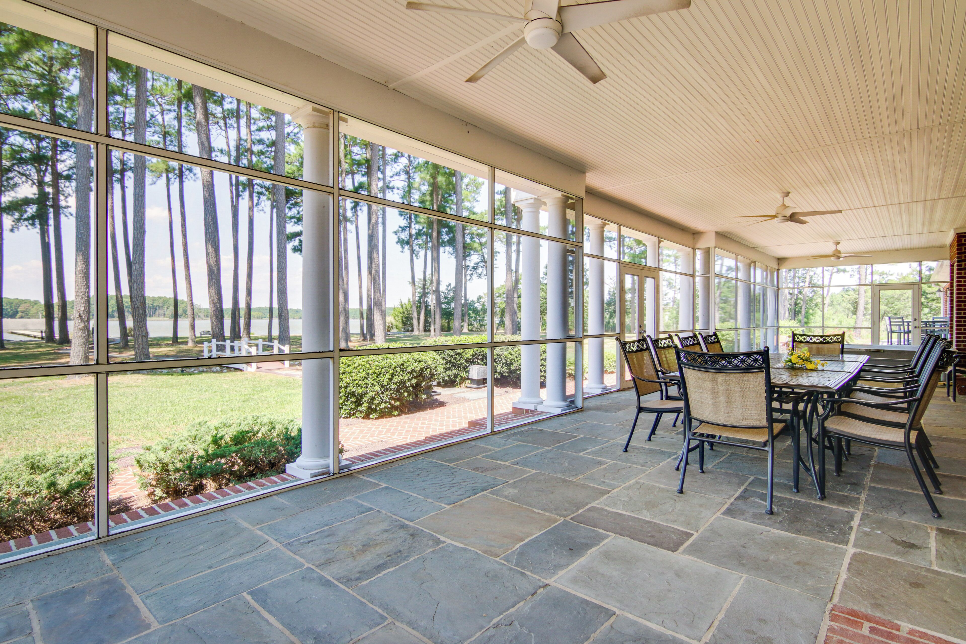 A covered patio with stone flooring, large windows, and outdoor seating.