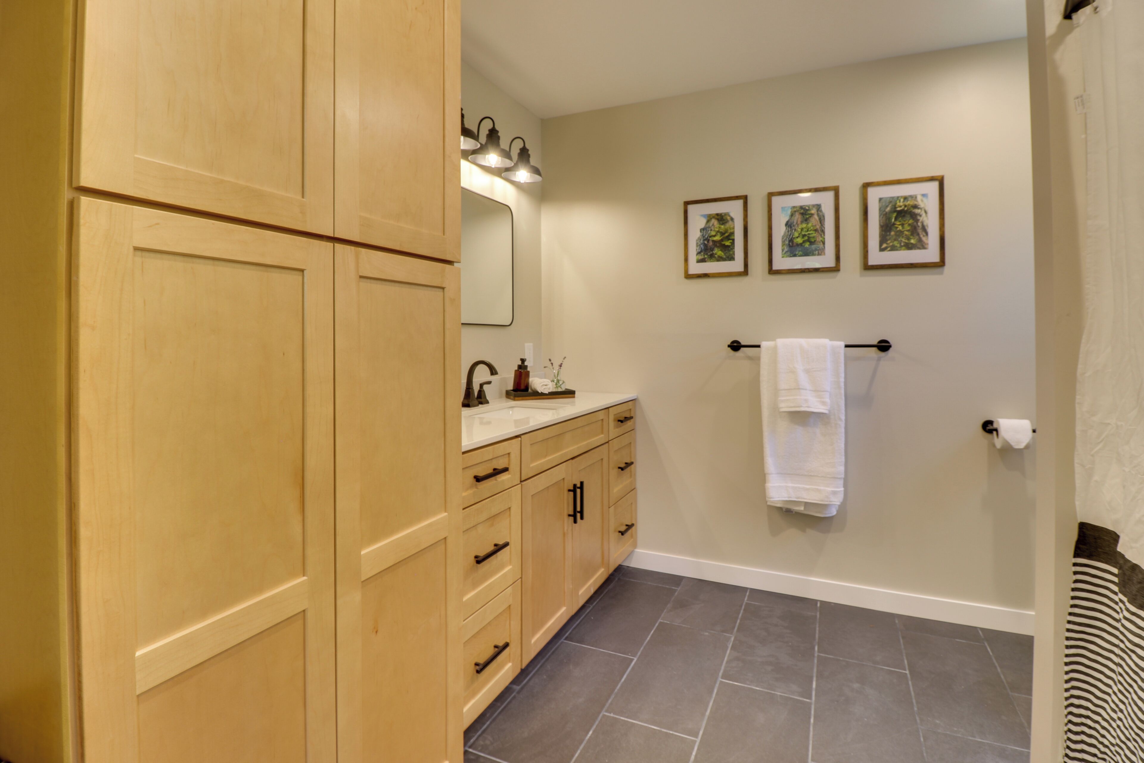 A bathroom with wooden cabinets, a sink, a mirror, and three framed pictures on the wall.