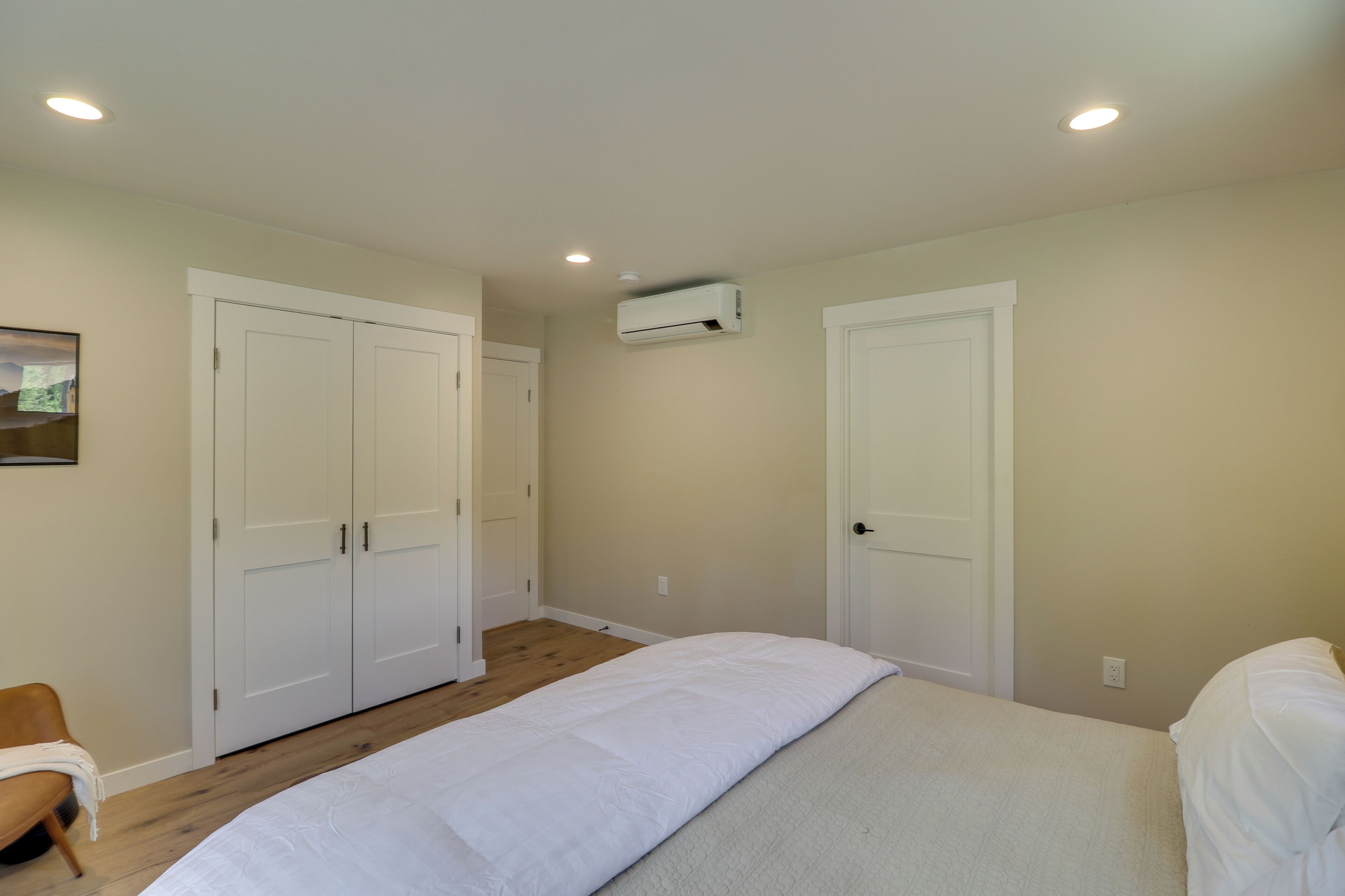 Un dormitorio con una cama, dos armarios, un aire acondicionado blanco y suelo de madera.
