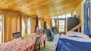 Ein gemütliches Zimmer mit Holzbalkendecke, einem Esstisch mit floralem Tischläufer, einer Couch, einem Bett und einer blauen Tür.