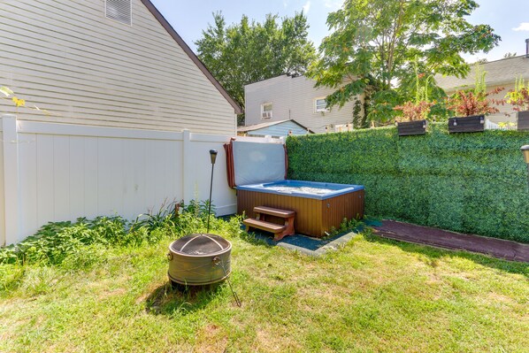 Un patio trasero con un jacuzzi, un banco de madera y un bote de basura.
