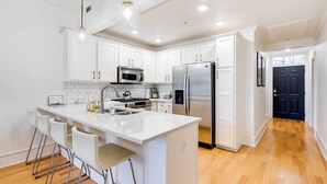 A modern kitchen with white cabinetry, stainless steel appliances, and a central island with bar stools. - Fayetteville Vacation Rental Near UA Campus (Fayetteville)