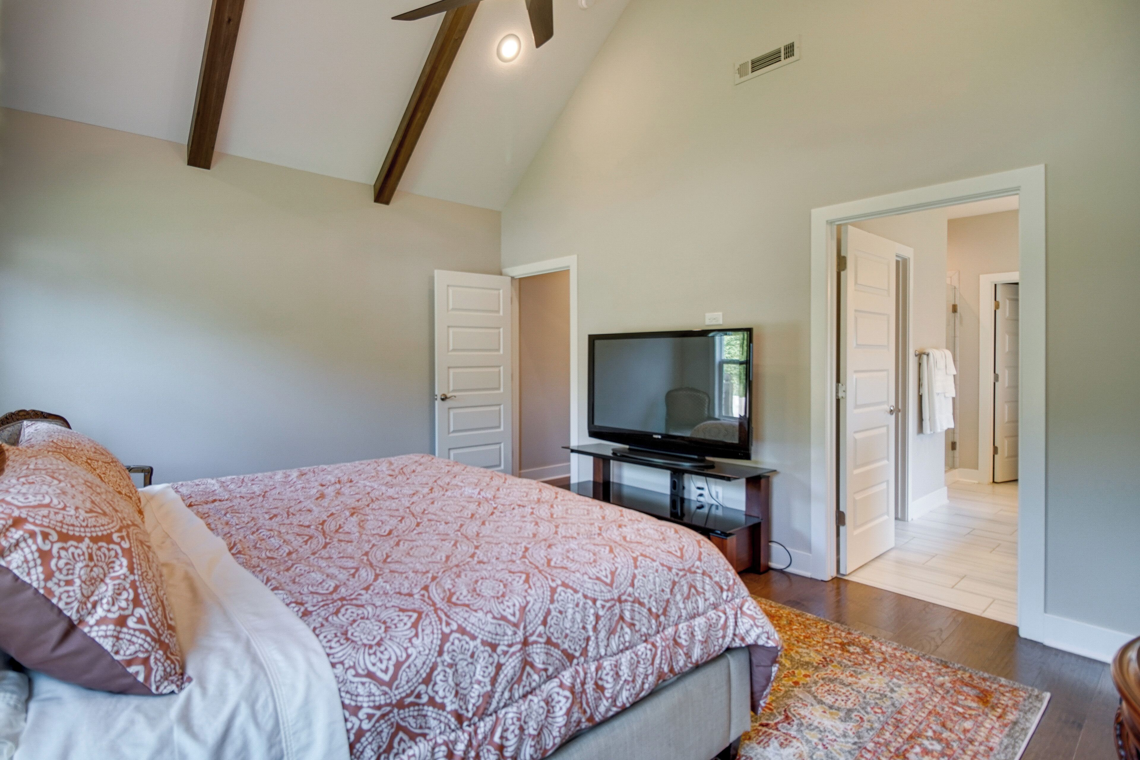 Une chambre avec un grand lit, un téléviseur posé sur un meuble, et un couloir menant à une autre pièce.