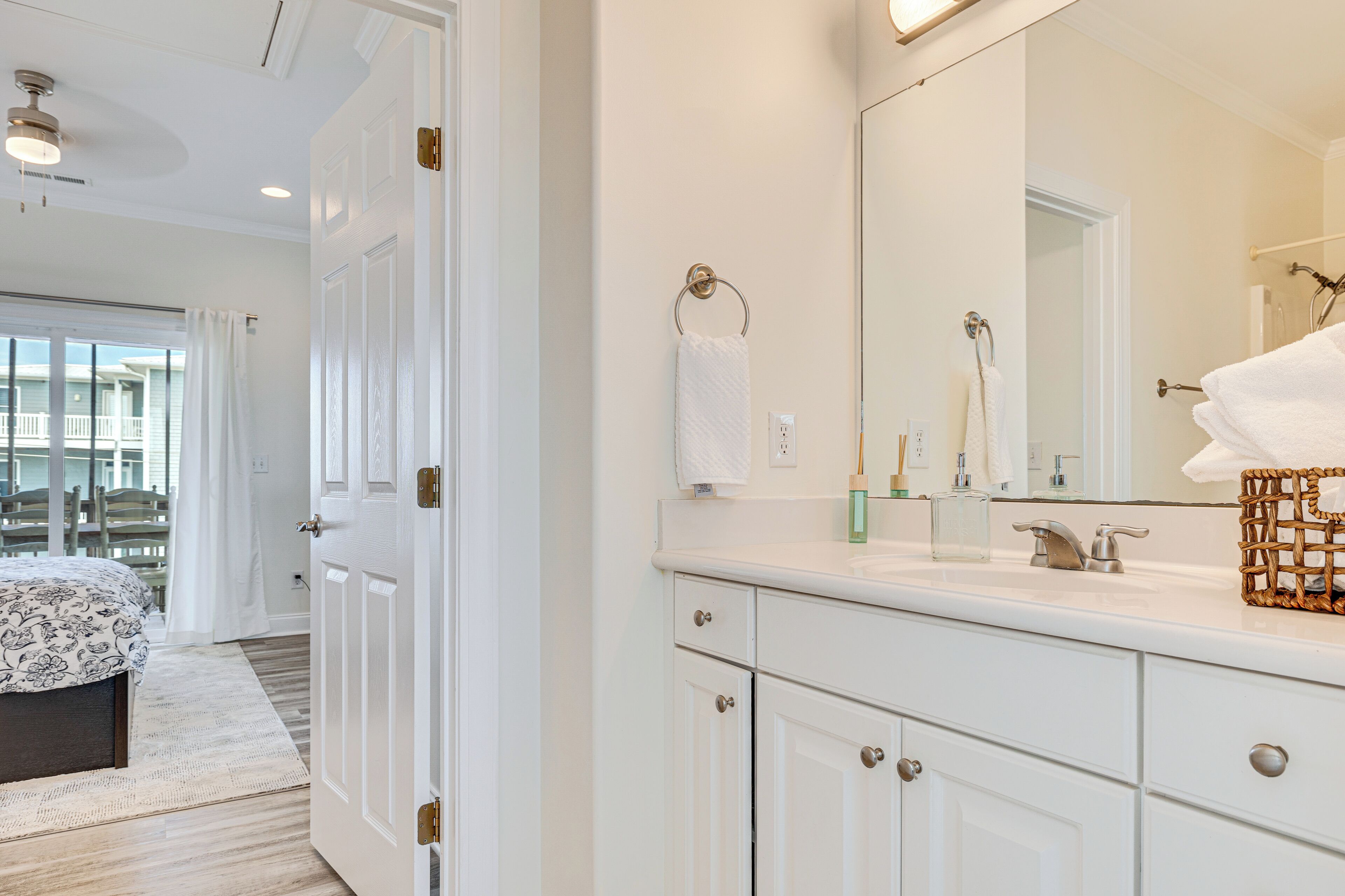 A hotel bathroom with a large mirror, white cabinets, and a sink.