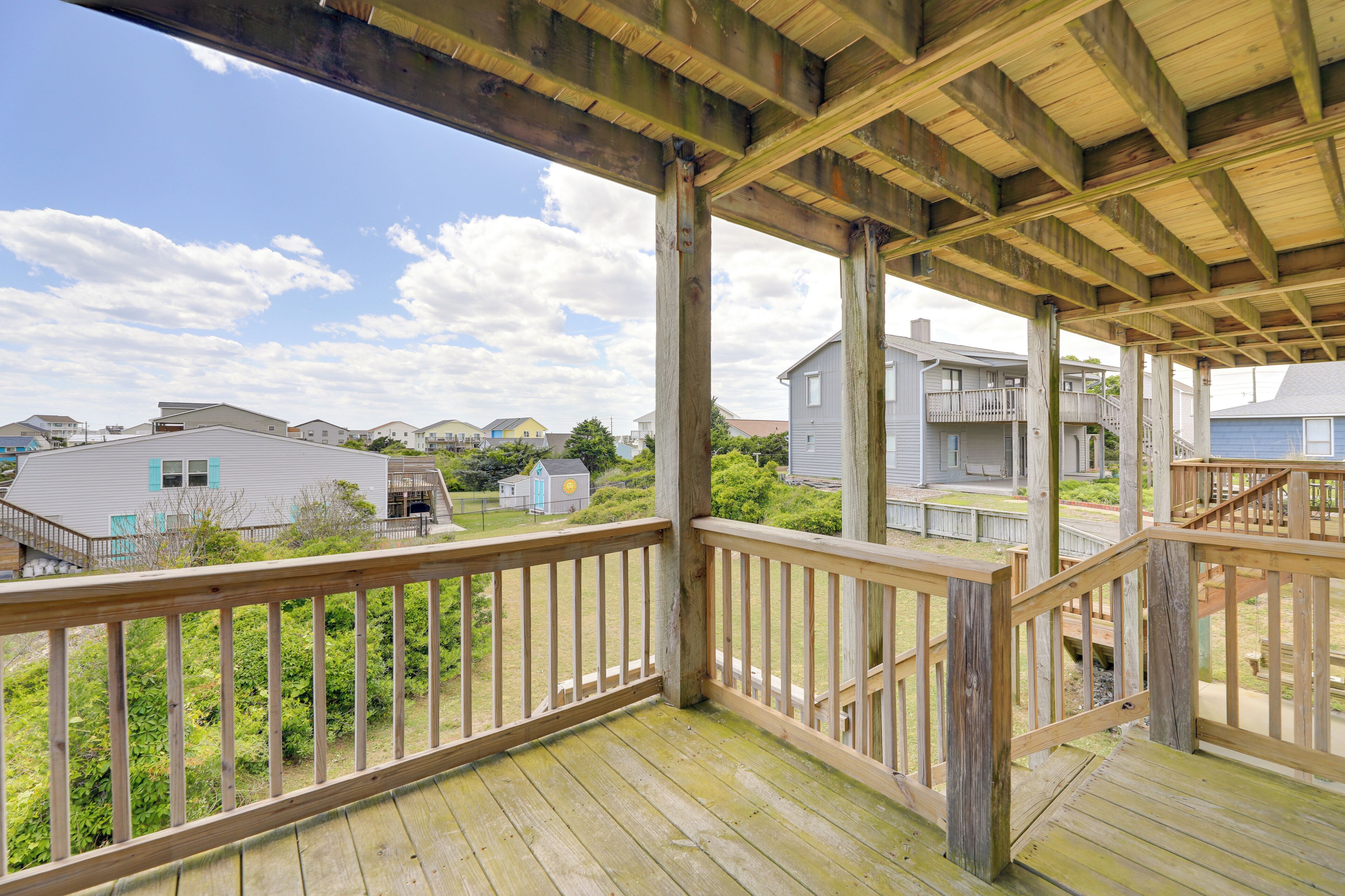 A wooden deck with railings, a staircase, and a view of residential houses.