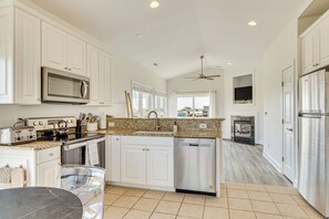A modern kitchen with white cabinets, stainless steel appliances, a granite countertop, and a view to the living area.