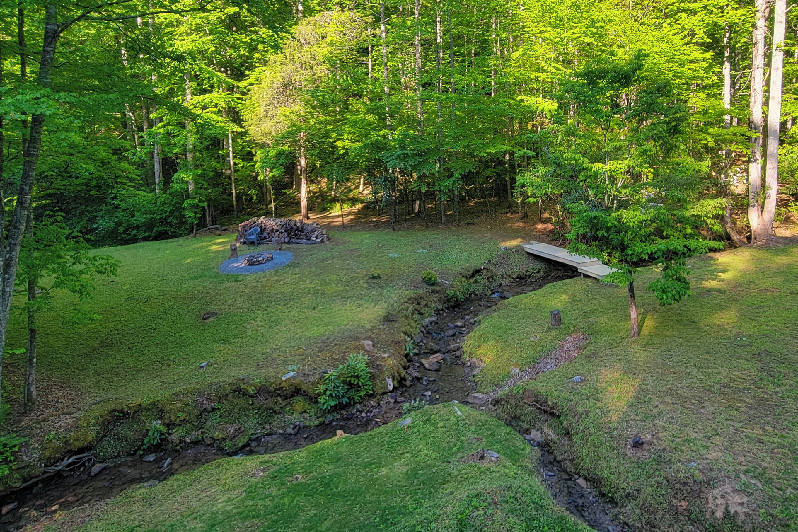 Une zone boisée avec un petit ruisseau, une pile de bois de chauffage et un pont en bois.