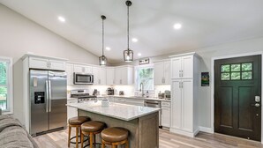 Cocina moderna con refrigerador de acero inoxidable, microondas, una isla grande con taburetes y una puerta de madera oscura.