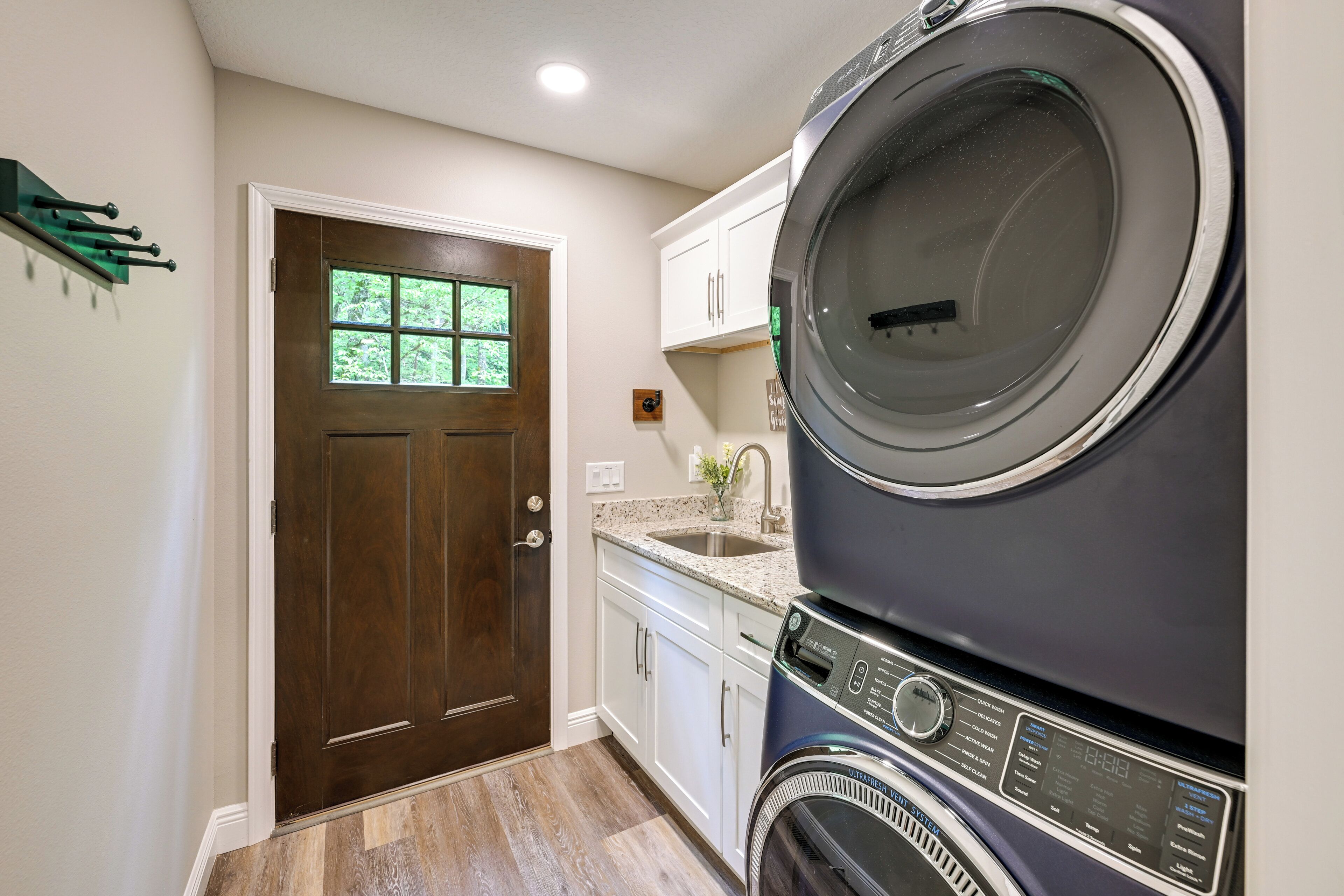 Une buanderie équipée d’un lave-linge et d’un sèche-linge à chargement frontal, d’une porte en bois et de meubles de rangement blancs.
