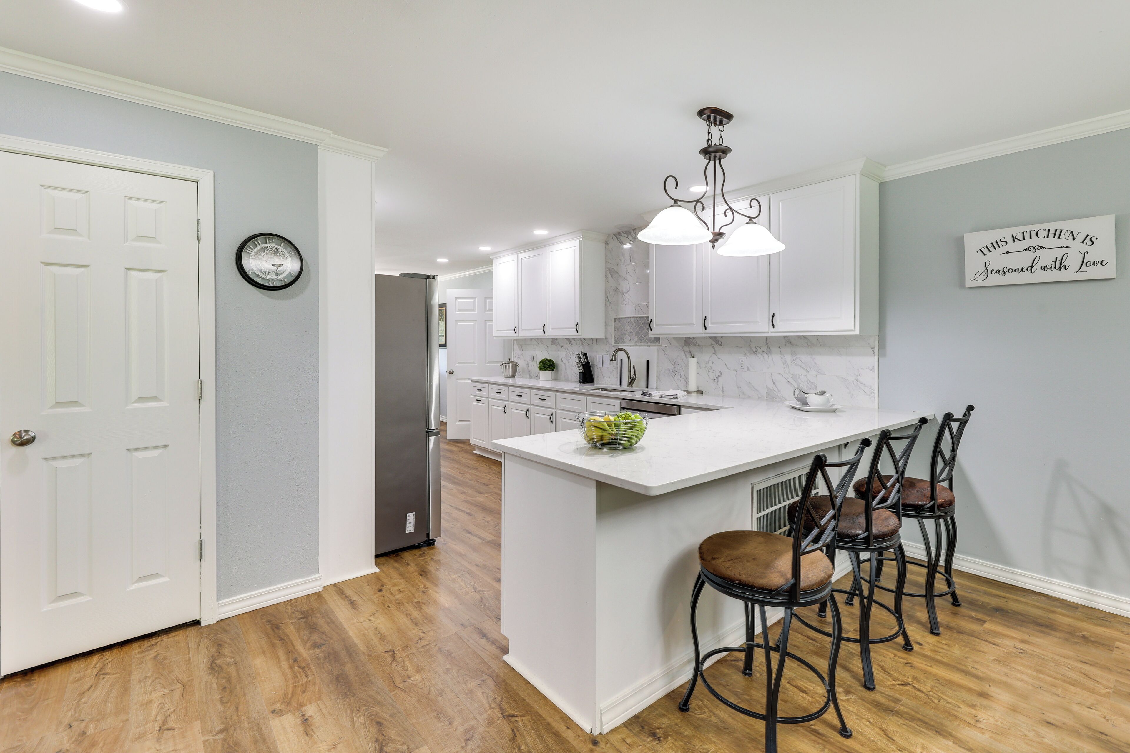 A modern kitchen with white cabinetry, a marble countertop, and a central island with bar stools.