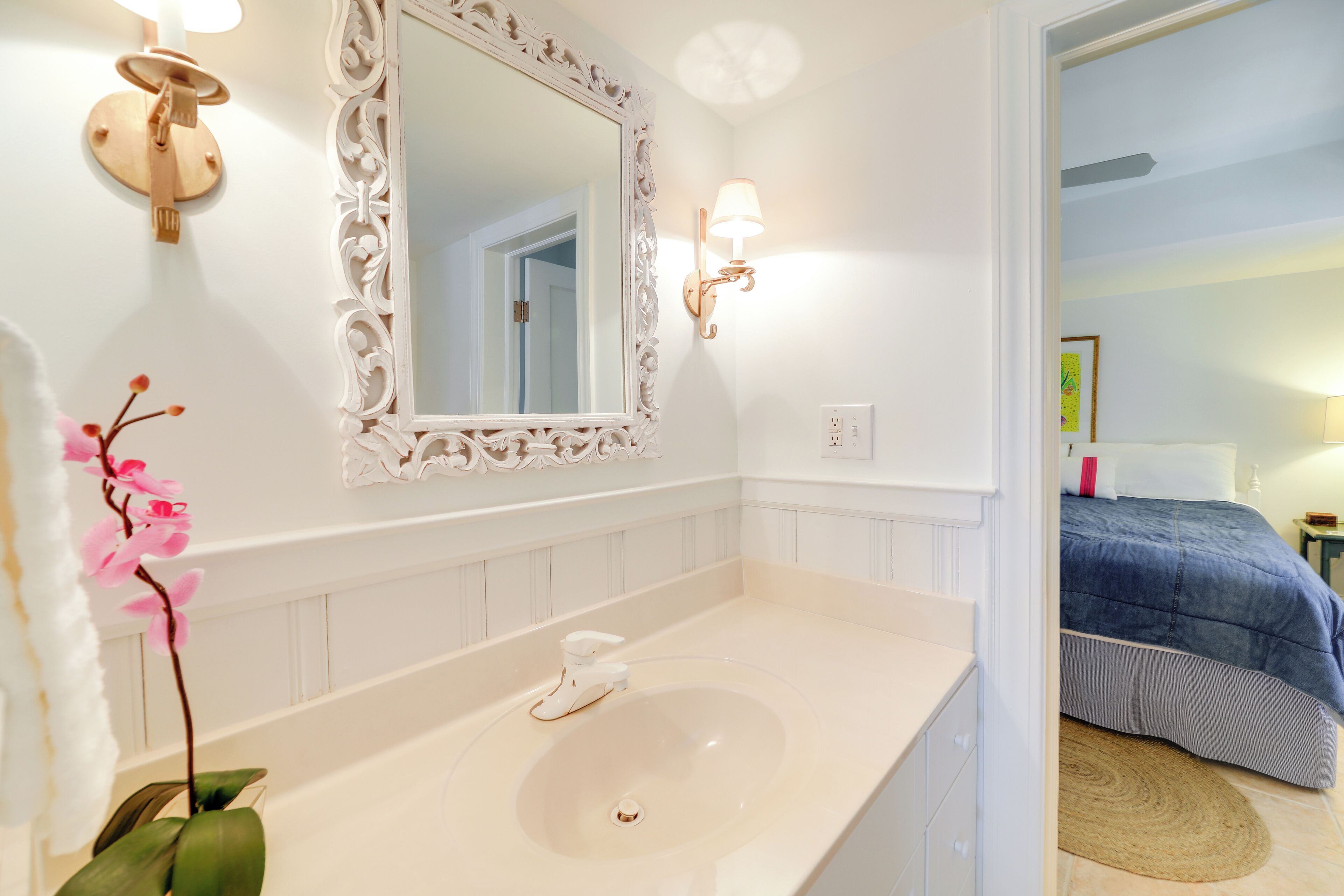 A bathroom with a white vanity, a large mirror, and a pink orchid plant.