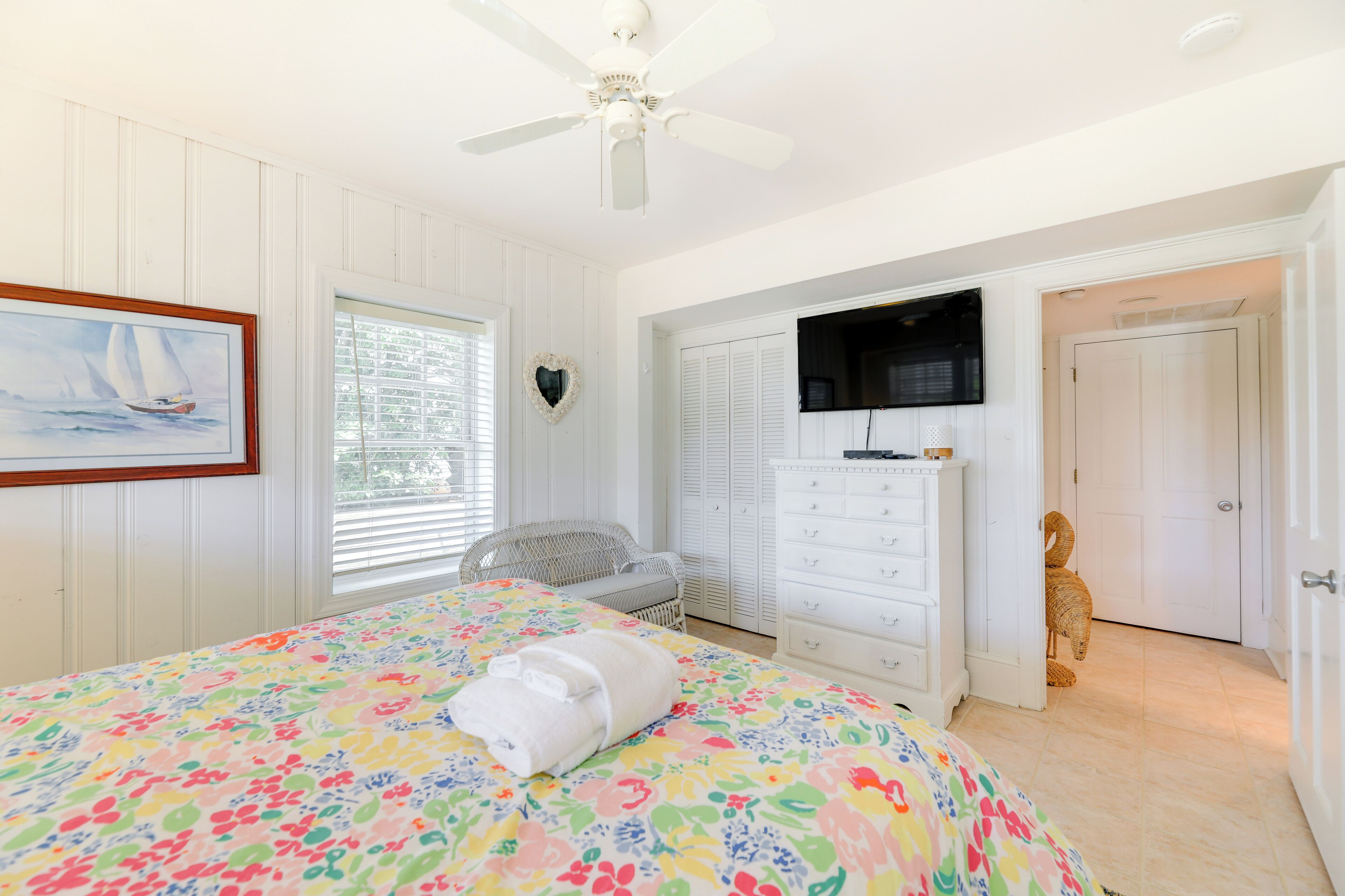 Un dormitorio con cama, cómoda, silla, televisor y puerta.