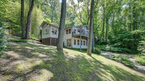 A two-story house with a balcony, surrounded by a forested area.