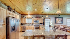 A spacious kitchen with wooden cabinets, granite countertops, stainless steel appliances, and a large island with bar stools. - Jefferson Vacation Rental With Golf Cart! (Jefferson)