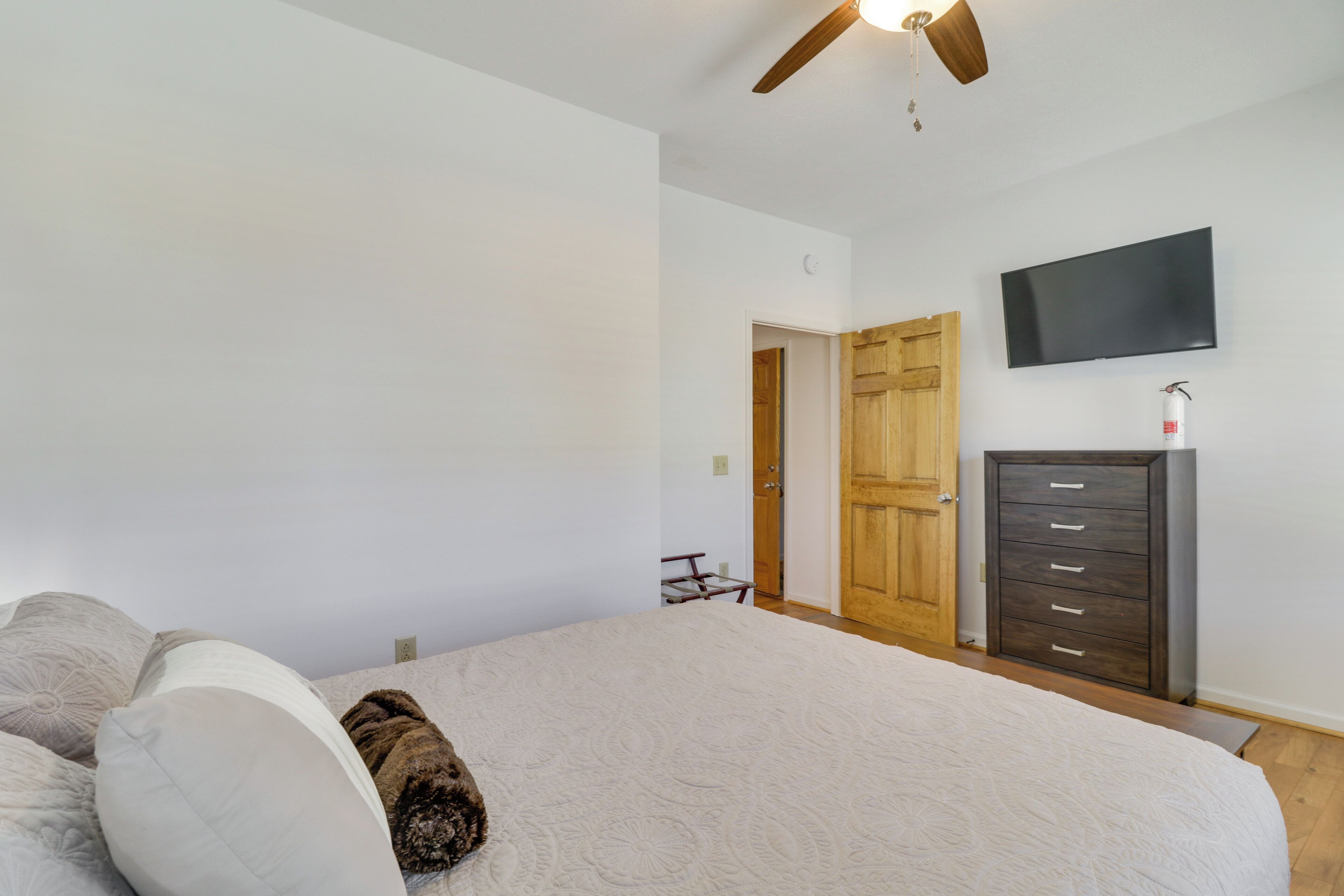 A bedroom with a bed, a wooden door, a dresser, and a TV mounted on the wall.