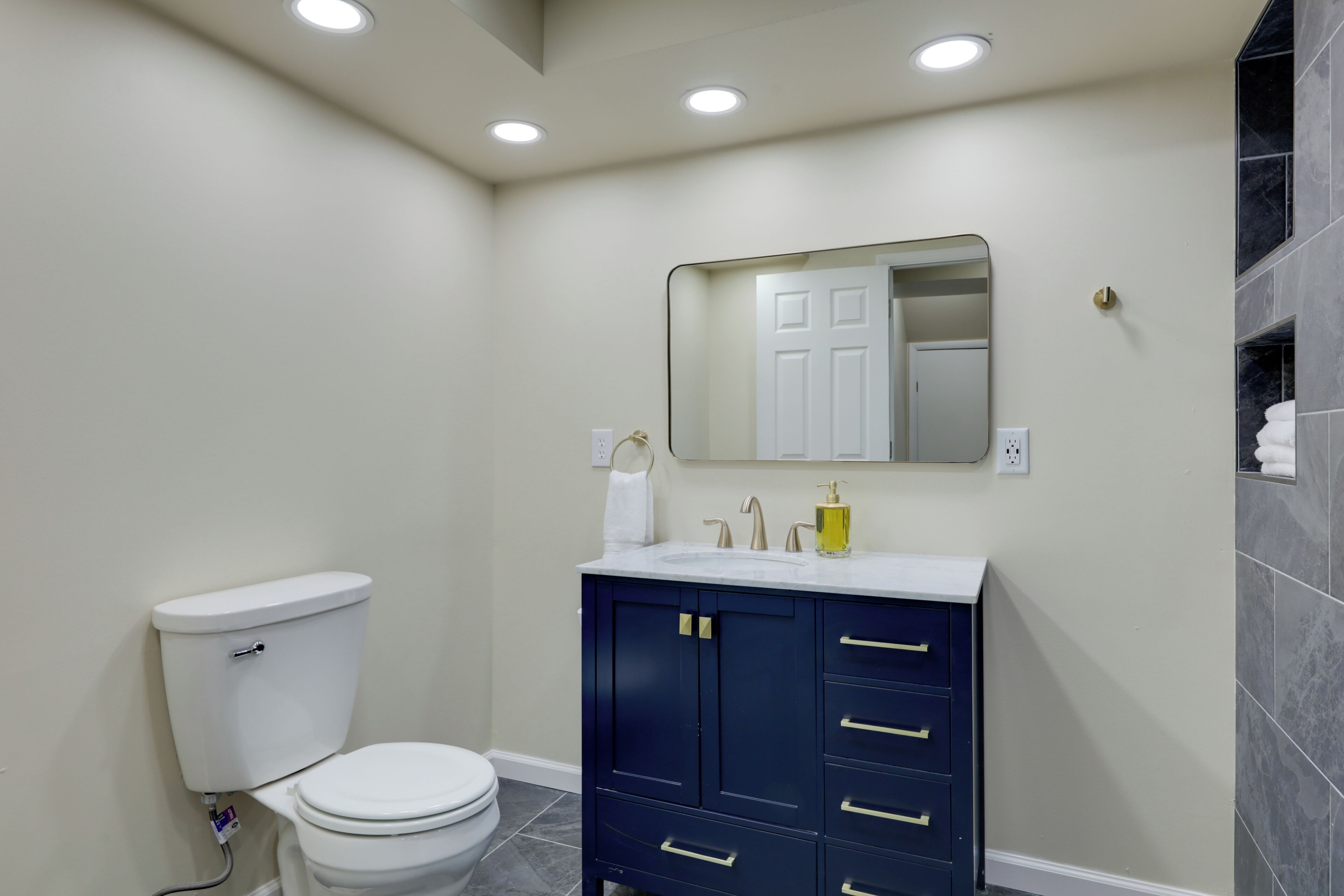 A bathroom with a white toilet, dark blue cabinet, and a mirror above the sink.