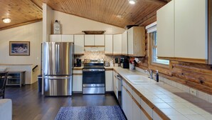 A modern kitchen with wooden ceiling beams, stainless steel appliances, and a large window providing natural light. - Cozy Brookville Home w/ Fire Pit & Deck! (Brookville)