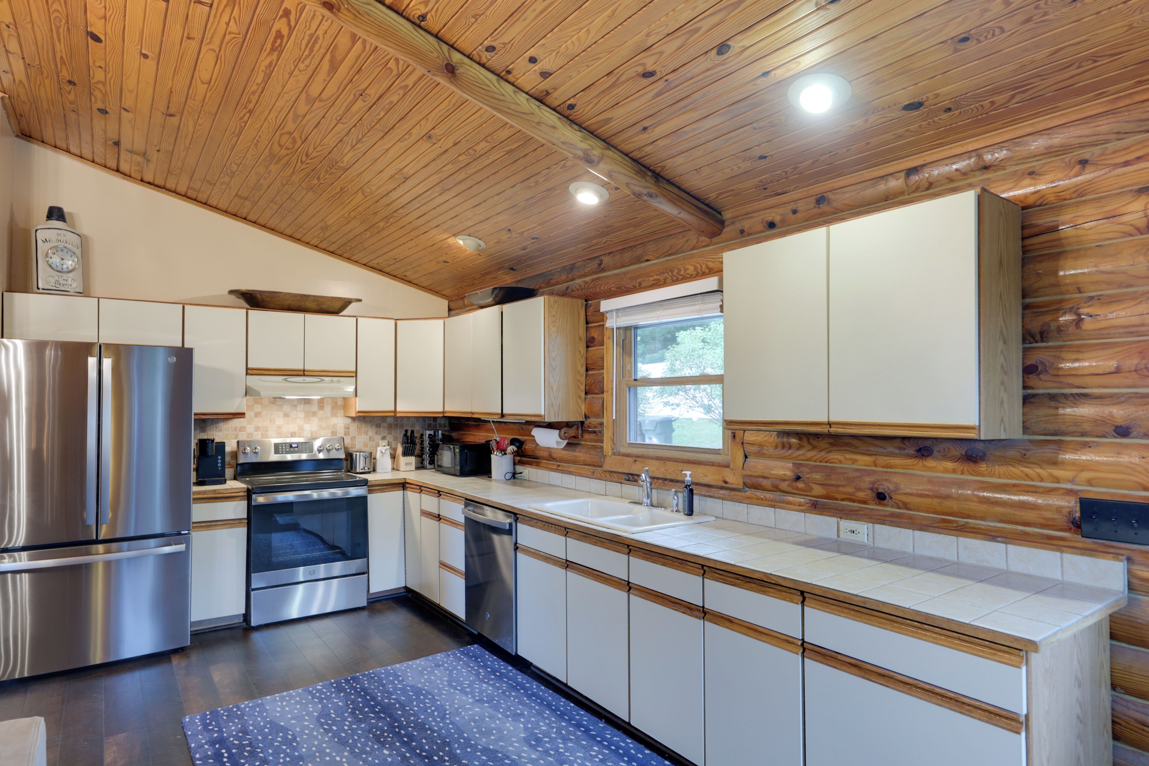 A modern kitchen with wooden ceiling beams, stainless steel appliances, and a large window.