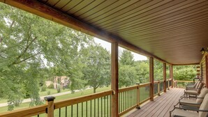 A covered outdoor deck with wooden railings and chairs, overlooking a grassy area with trees. - Cozy Brookville Home w/ Fire Pit & Deck! (Brookville)