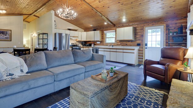 A cozy living room with a sofa, a coffee table, and a leather armchair. There is a kitchen in the background with cabinets and a refrigerator. - Cozy Brookville Home w/ Fire Pit & Deck! (Brookville)