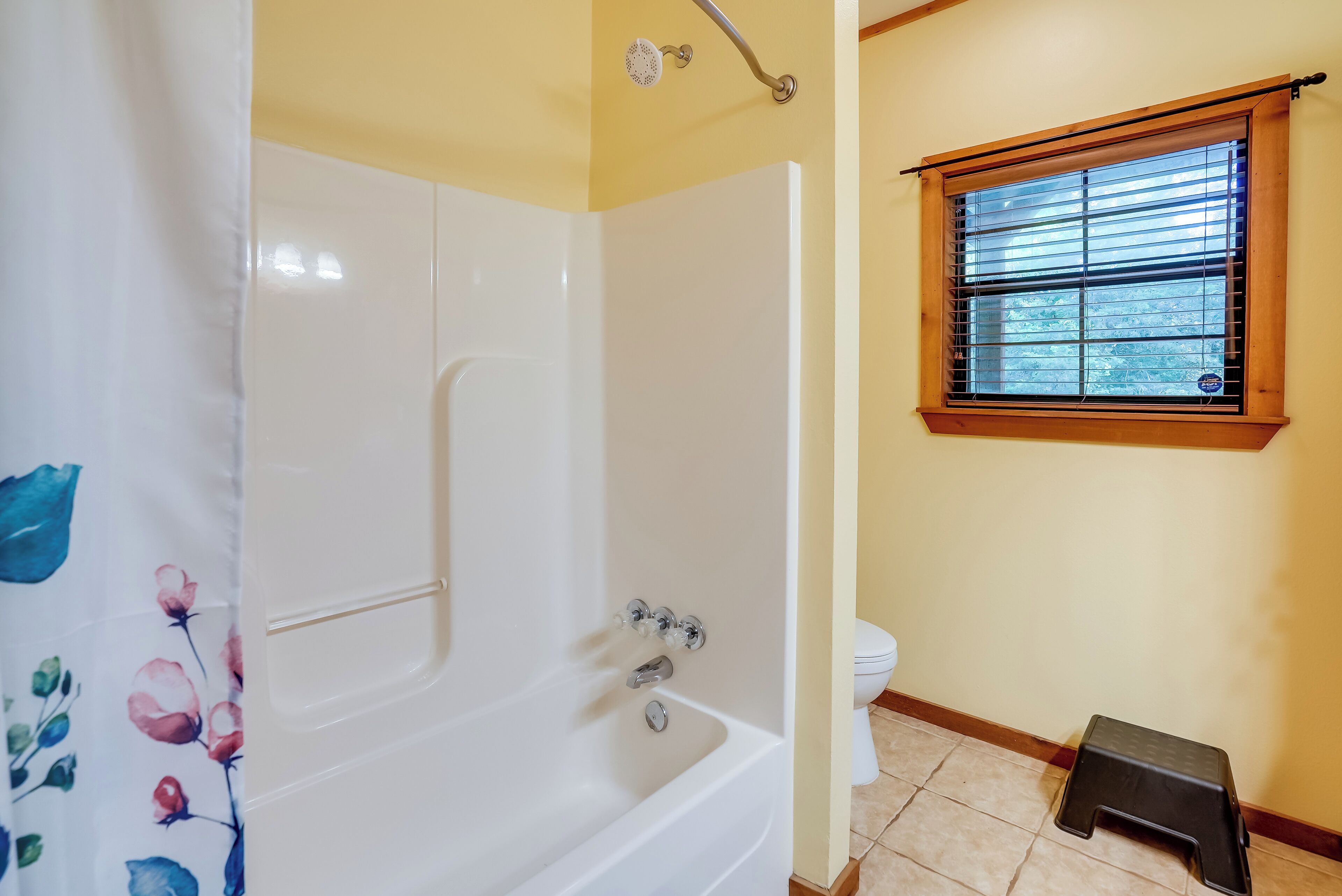 Un bagno con una vasca da bagno bianca, una doccia, un water e una finestra con persiane.