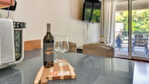 Een keukenblad met een fles wijn en twee glazen, een aan de muur bevestigde televisie, en een schuifdeur naar een buitenruimte.