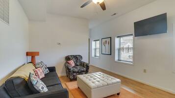 A spacious living room with a ceiling fan, a sofa, an ottoman, a chair, and a TV mounted on the wall.