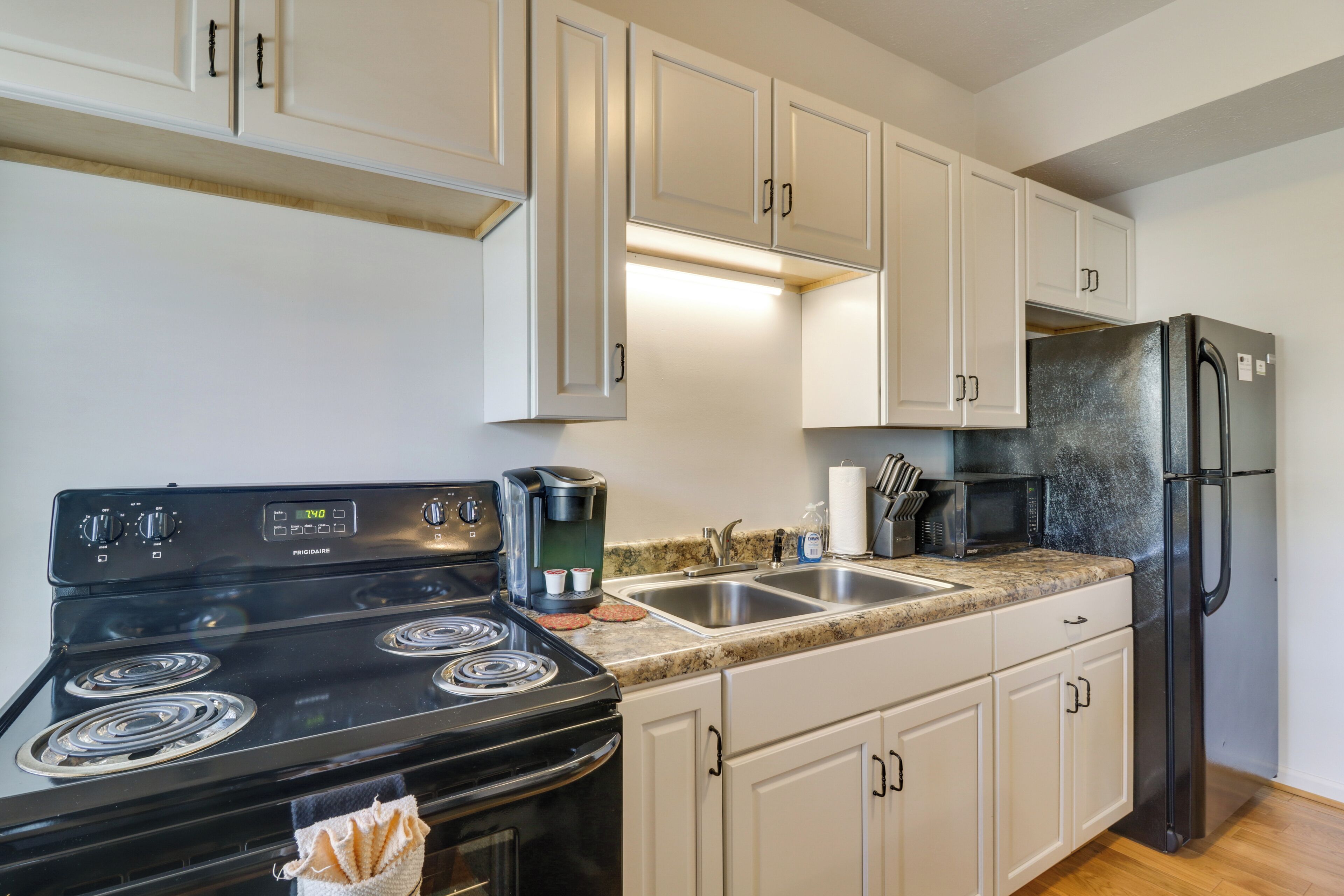 A kitchen with white cabinets, a black stove, a refrigerator, and a microwave.