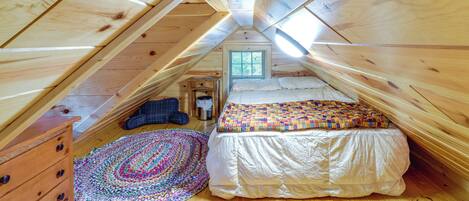 A cozy attic bedroom with a wooden ceiling, a bed with a colorful quilt, a wooden dresser, and a patterned rug.