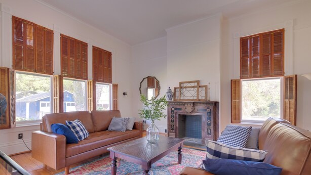 A living room with a brown leather sofa, a matching armchair, a coffee table, and a patterned rug. There is a fireplace with a mantel and a mirror above it. - WFH Friendly: Abode w/ Balcony in Columbus! (Columbus)