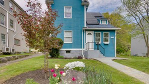 A two-story house with a blue exterior, a front porch, and a garden with various flowers and a tree. - Pet-friendly Connecticut Retreat Near Golfing! (Waterbury)