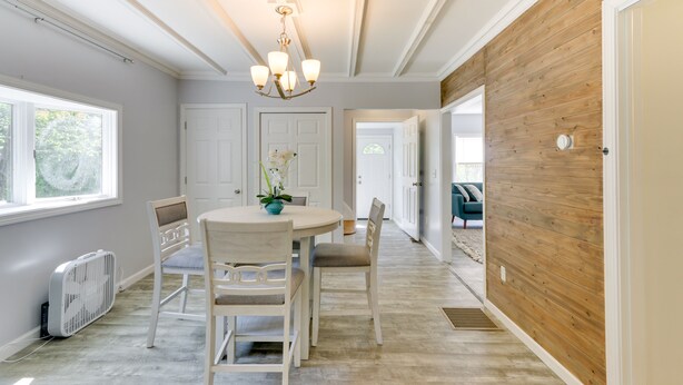 A dining area with a round table, chairs, and a chandelier. There are white doors and a wooden wall in the background. - Pet-friendly Connecticut Retreat Near Golfing! (Waterbury)