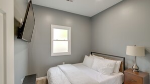 Ein Schlafzimmer mit einem Bett, einem Nachttisch, einer Lampe, einem an der Wand montierten Fernseher und einem Fenster.