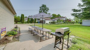 Ein Garten mit Picknicktischen, einem Grill und einem gestreiften Sonnenschirm.