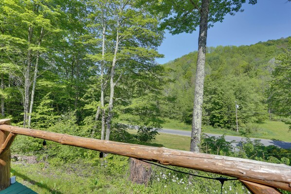 A wooden deck with a view of a forested area and a road in the distance. - Private Cabin Rental in the Catskill Mountains! (Hamden)